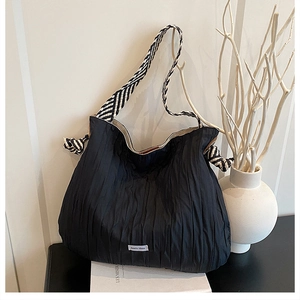 Détail du sac cabas en tissu plissé noir avec bandoulière tissée rayée sur support épuré