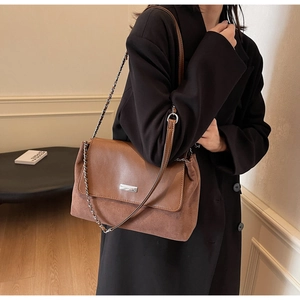 Detail view of brown patchwork leather shoulder bag featuring silver metal nameplate