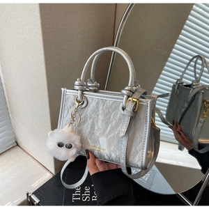 Close-up of silver textured handbag with soft plush charm and dual handles