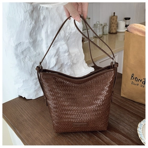 Detailed view of dark brown woven leather bucket bag texture on a wooden table