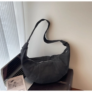 Close-up of black quilted dumpling bag with silver zipper in minimalist office setting