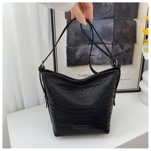 Close-up of black woven bucket bag with metal logo detail on a bright modern desk