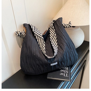 Détail d'un sac cabas plissé noir avec anses ruban rayées dans un décor intérieur élégant