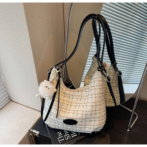 Close-up of cream tweed crescent bag with black leather straps and plush toy charm