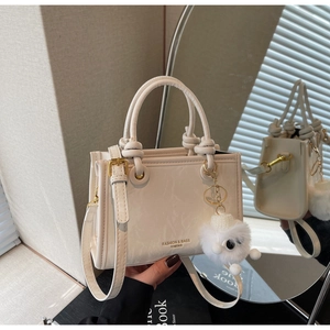 Detail of cream bucket bag with elegant dual handles and matching plush charm decoration