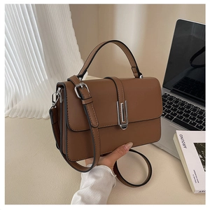Brown leather handbag with silver vertical clasp and adjustable strap on office desk