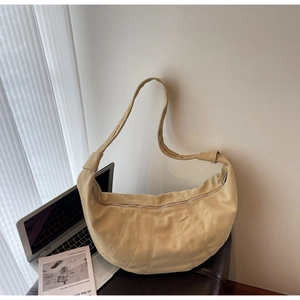 Detail of a beige suede croissant bag featuring stitched leather panels and a metal zipper