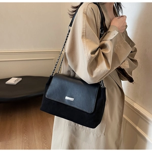 Detail of black leather and suede crossbody bag with silver metal chain and plaque