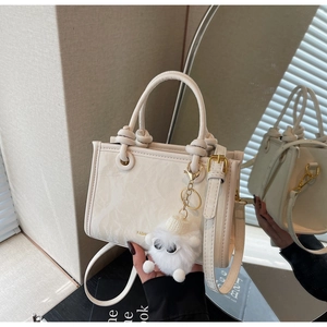 Detail of white bucket bag with cloud texture, knotted handle, and plush charm