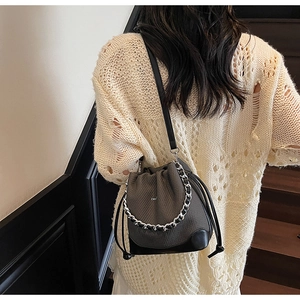 Detail of a grey woven bucket bag with black leather base and stylish chain strap