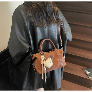 Detail of a brown Boston style bag featuring a plush bear charm and leather handles
