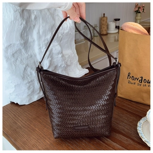 Close-up of a dark brown woven bucket bag with checkered texture on a wooden table