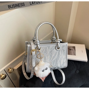 Detailed view of metallic silver bucket bag with pleated texture and plush charm