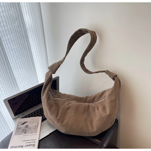 Close-up of brown suede croissant bag with decorative stitching on a desk