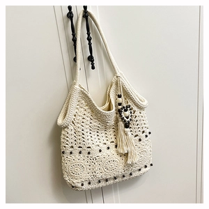 Detail of hand-woven cream tote bag featuring hollow patterns, wooden beads, and a tassel charm