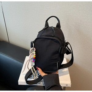 Detail of black nylon crossbody bag featuring stylish multi-element pendant and woven tag