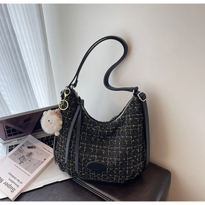 Close-up of black tweed shoulder bag with gold thread detail and white fur ball charm