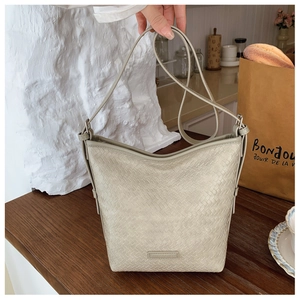Detail of woven texture bucket bag in beige with adjustable strap and embossed logo