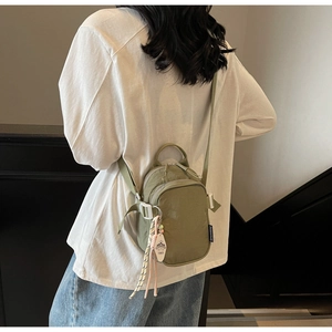 Detail of light army green nylon mini crossbody bag with layered zippers and pendant tag