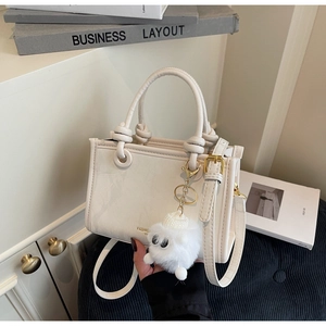 Detail of cream leather tote bag with knot handle and plush ball charm in a stylish setting