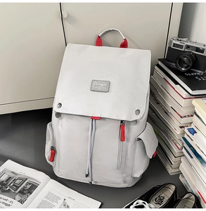 Light grey canvas backpack detail with red zippers, shown in a lifestyle scene with books
