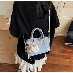 Detail of light blue pleated handbag with teddy bear charm shown on female model
