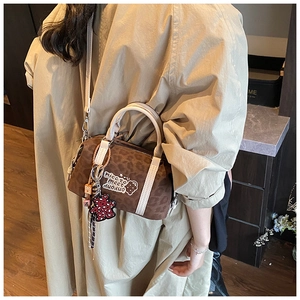Detailansicht der braunen Boston-Tasche mit Leopardenmuster, Stickerei und Anhängern am Model