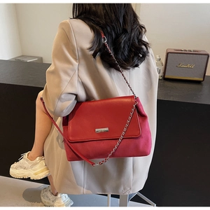 Detail of red mixed leather shoulder bag featuring metal chain and engraved brand plate