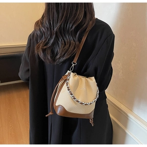 Detail view of woven bucket bag with cream straw texture, brown leather trim and silver chain