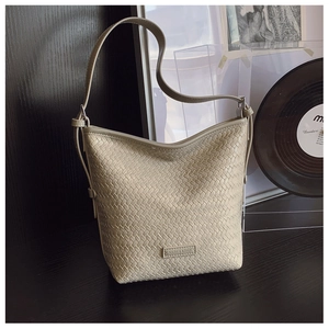 Detail view of a beige woven bucket bag with adjustable strap on a dark wooden table