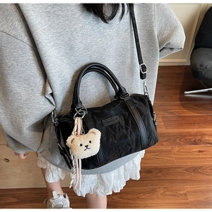 Close-up of black pleated Boston bag featuring a plush bear pendant and brand logo