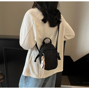 Rear view of a model wearing a minimalist black nylon mini backpack with a decorative tag