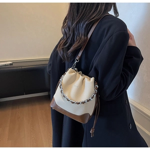 Detail of a beige canvas bucket bag with brown leather trim and metal chain handle
