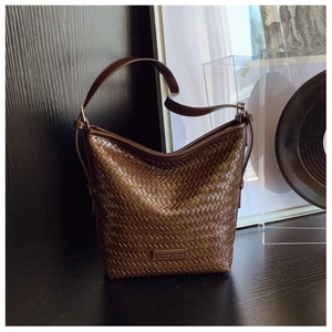 Detail of dark brown woven leather bucket bag with silver buckle and smooth strap