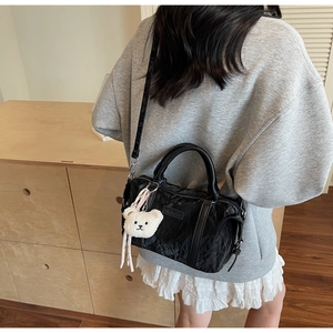 Detail of black wrinkled texture handbag with plush bear charm worn by a model