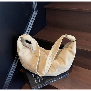 Macro shot of beige canvas croissant bag featuring curved quilted stitching and knotted strap