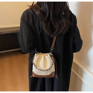 Detail view of woven bucket bag with brown leather trim and silver chain shoulder strap