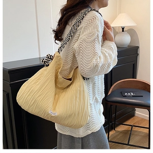 Détail du sac fourre-tout plissé jaune avec bandoulière rayée noir et blanc sur modèle