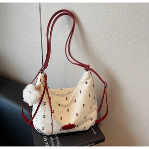 Detail of canvas tote bag featuring red bow prints and a white fuzzy pompom charm accessory