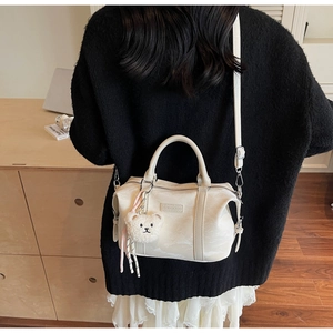 Creamy white Boston bag shown on model's shoulder with cute plush bear charm detail