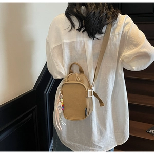 Detail of khaki crossbody mini bag with colorful charm on minimalist background