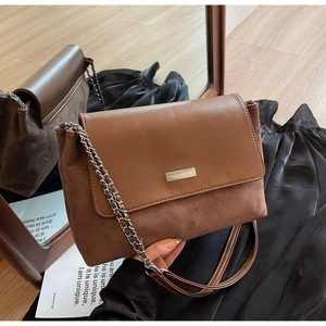 Detail of a brown leather shoulder bag with chain strap and silver metal logo on suede