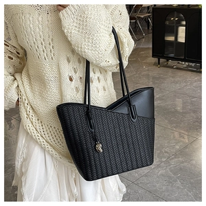 Detail of black woven leather tote bag with elegant heart charm worn by a model