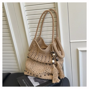 Detail of bohemian woven tote bag with hollow pattern and decorative tassels on leather surface