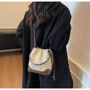 Detail shot of a woven cream bucket bag with brown leather trim and silver chain on model