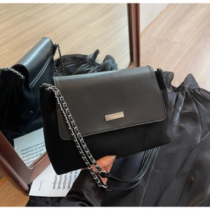 Close-up of black crossbody bag with mixed textures, gold metal plate and chain strap