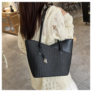 Close-up of black woven tote bag with silver heart charm and smooth leather trim