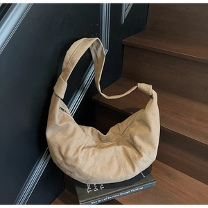 Detail of khaki suede crescent bag with knotted strap and zipper on wooden steps