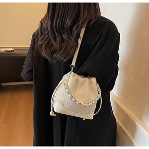 Detail of beige bucket bag featuring diamond quilted texture and silver chain strap