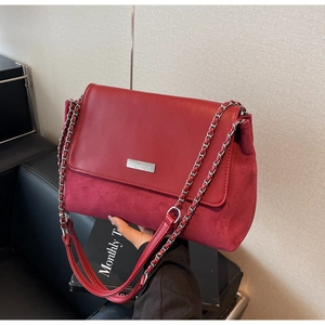 Close-up of red mixed-texture shoulder bag with silver logo plate and chain strap